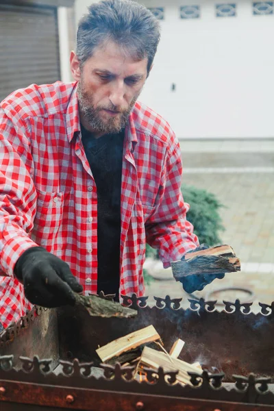 Man with beard puts firewood in fire mangala — Stock Photo, Image