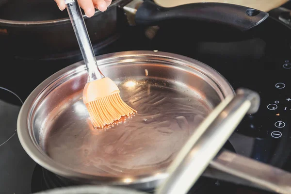 Кухонная щетка смазывает черную сковородку маслом — стоковое фото