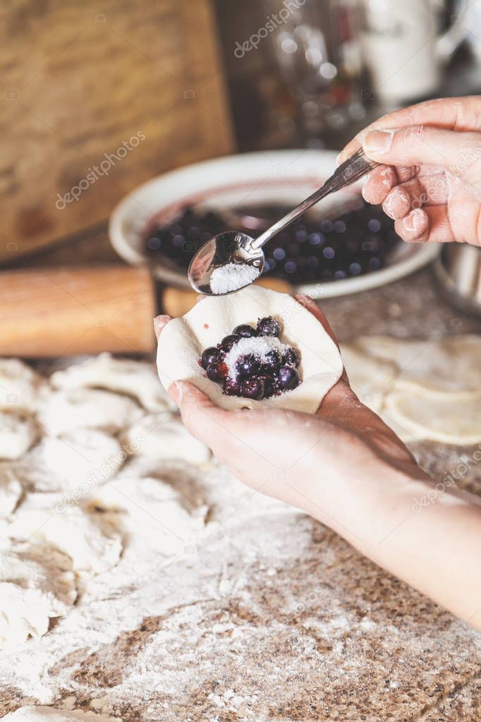Hand of woman pouring sugar into dumpling with black berries
