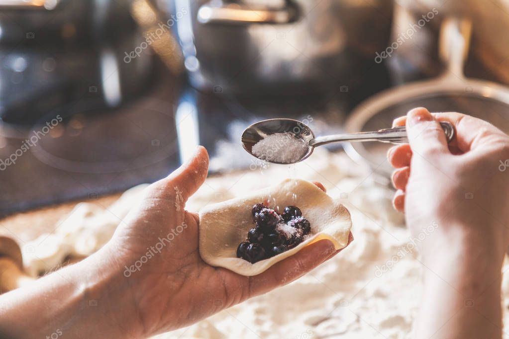 Hand of woman pouring sugar into dumpling with black berries