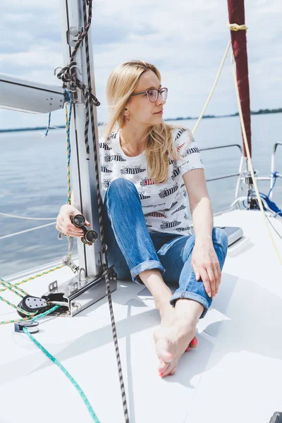 Slender barefooted blonde in spectacles sits on nose of yacht — Stock Photo, Image