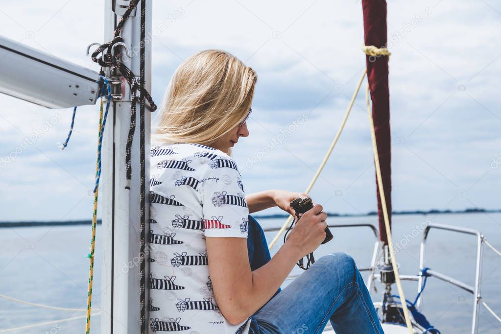 slender blonde in jeans sits on nose of white yacht