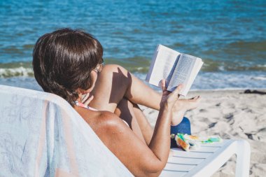 Yaşlı kadın plajda kitap okuma