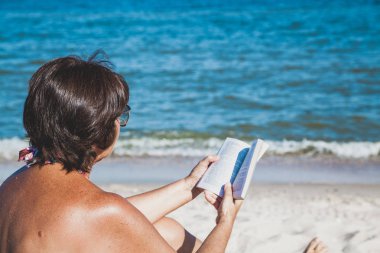 Yaşlı kadın plajda kitap okuma