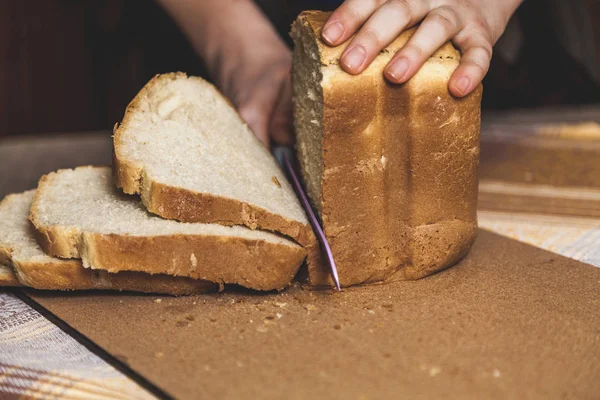 woman hands slice fresh bread slices with knife.