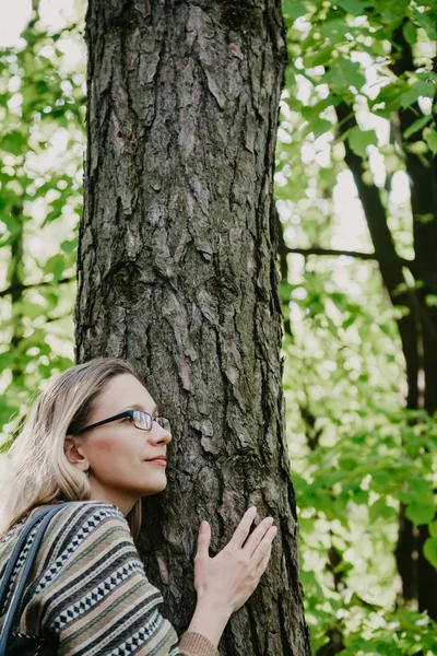 Λεπτή ξανθιά με τα γυαλιά που αγκαλιάζει κορμό δέντρου — Φωτογραφία Αρχείου