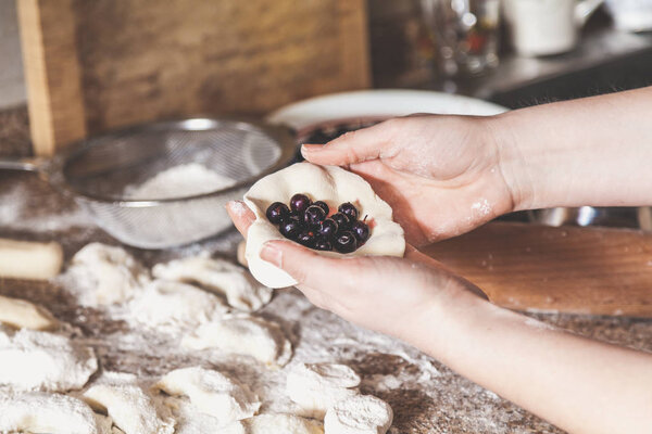 hands of  woman make dumpling with black berries