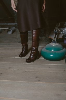 Deri çizmeli kadın bacakları tahta zeminde duruyor.