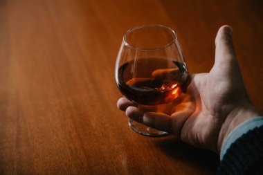 Elleri bardağı konyakla yakın plan tutuyor.