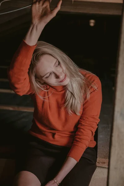 Bionda in maglione arancione si siede su sfondo scuro — Foto Stock