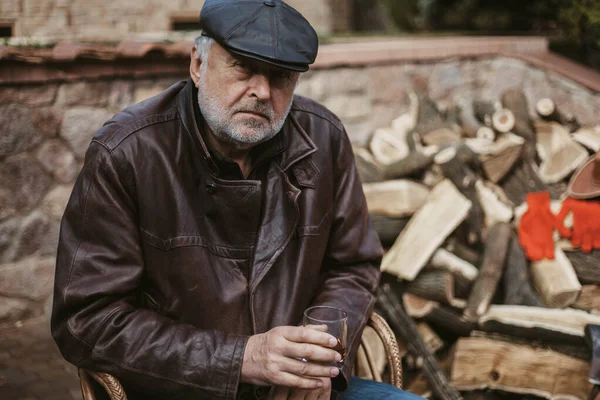 Anciano con barba en chaqueta de cuero se sienta en el patio — Foto de Stock