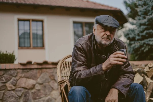 Anciano con barba en chaqueta de cuero se sienta en el patio — Foto de Stock