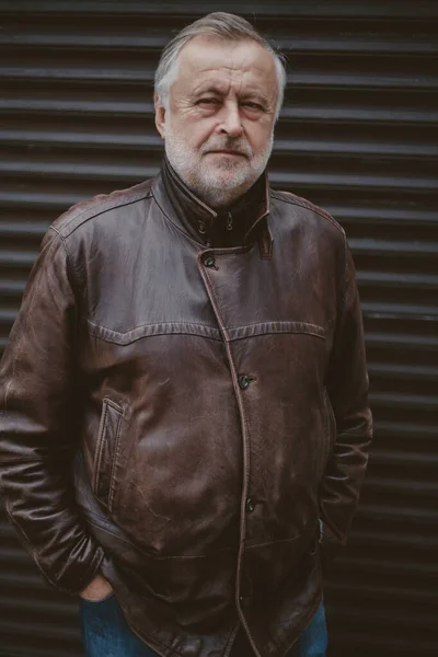 Handsome elderly man in leather jacket stands in front gate