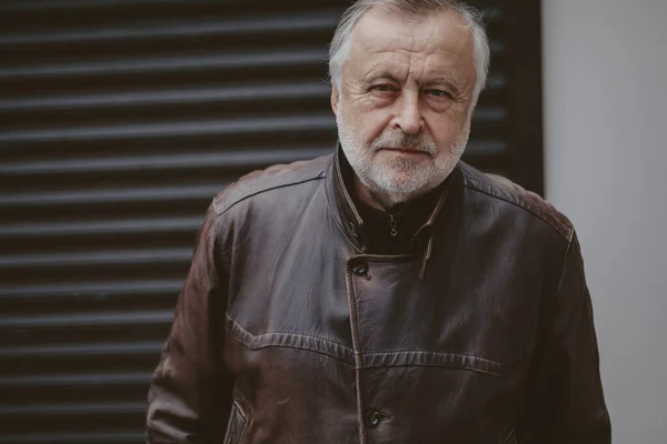 Handsome elderly man in leather jacket stands in front gate