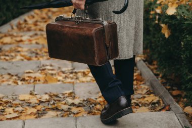 Halı çantalı ve ceketli bir adam sonbahar caddesinde yürüyor.