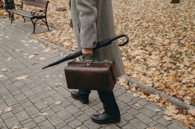 Halı çantalı ve ceketli bir adam sonbahar geçidi boyunca yürür.