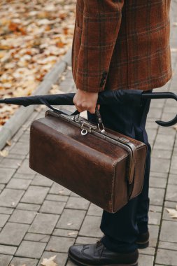 Sonbahar parkının arka sokağında ceketli bir adam duruyor.