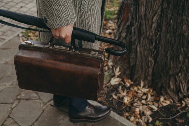 Halı çantası ve şemsiye bastonu elinde palto giymiş bir adamın.