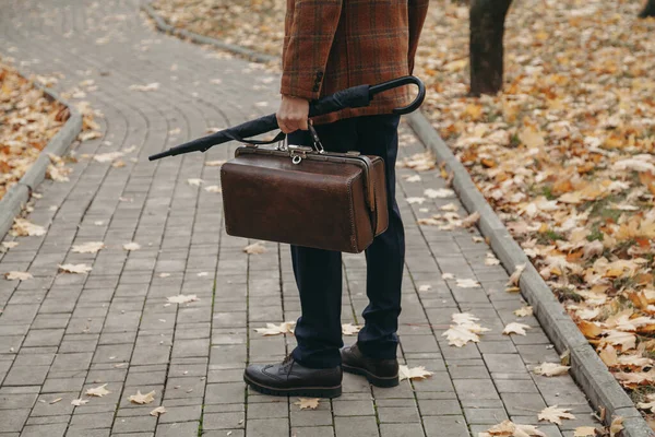 Άνδρας με carpetbag στο σακάκι στέκεται στο σοκάκι του φθινοπώρου πάρκο — Φωτογραφία Αρχείου