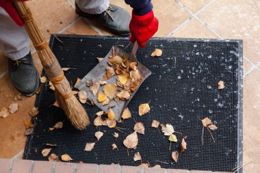 Sahibi dökülen yaprakları kauçuk paspastan temizler
