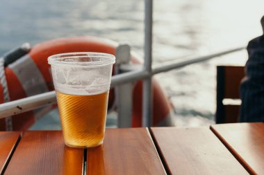Plastic glass with beer is on table on board ship clipart