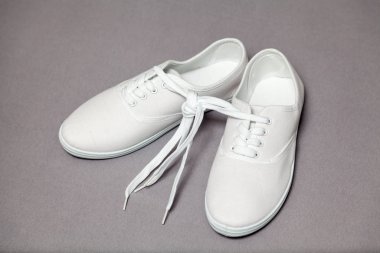 Gri arka planda duran beyaz spor ayakkabıları çifti