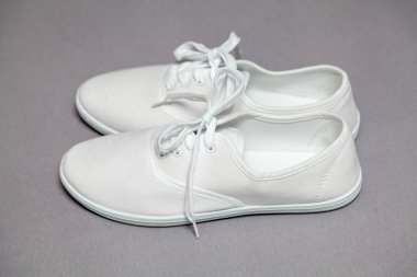 Gri arka planda duran beyaz spor ayakkabıları çifti