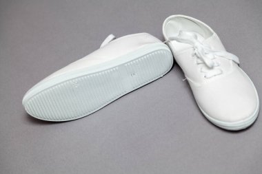 Gri arka planda duran beyaz spor ayakkabıları çifti