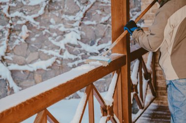 İşçi verandadaki karı uzun fırçayla temizler