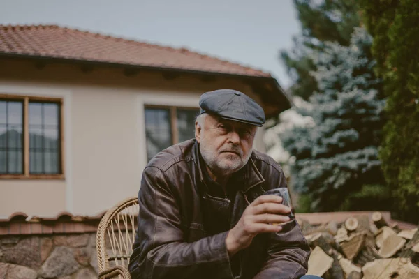 Elderly man with beard in leather jacket sits in yard — Stock Photo, Image