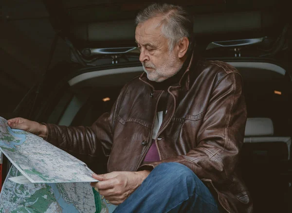 Hombre mayor en chaqueta de cuero está estudiando mapa en coche — Foto de Stock