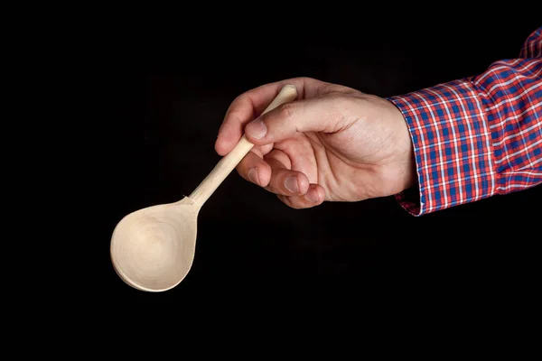 Hand holds wooden spoon on black background