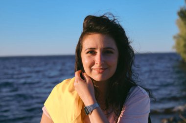 Uzun kızıl saçlı hoş bir kız su yüzeyinin arka planında duruyor. Doğal kusurlarıyla rötuş yapmayan bir kadının portresi