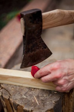 Balta ve çilek. Bir el, olgun kırmızı bir çileği baltayla kesiyor.