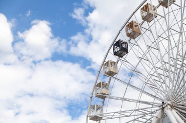 Çekiciliğe bakıyorum. Dönme dolapta beyaz bulutlu mavi gökyüzüne karşı kulübeler.