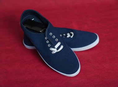 Beyaz tabanlı ve bağcıklı iki yeni mavi spor ayakkabı kırmızı izole bir arka planda duruyor.