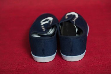 Beyaz tabanlı ve bağcıklı iki yeni mavi spor ayakkabı kırmızı izole bir arka planda duruyor.