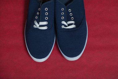 Beyaz tabanlı ve bağcıklı iki yeni mavi spor ayakkabı kırmızı izole bir arka planda duruyor.