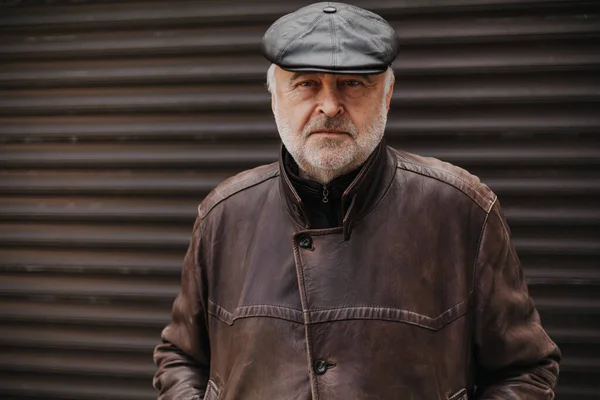 Portrait of a man with a gray beard. Close-up of an elderly man in a leather jacket and cap on an autumn day. Rear Rolling Gate