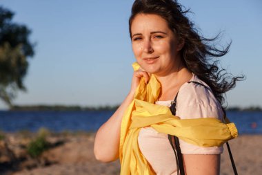 Güzel bir viraj portresi artı uzun kızıl saçlı uzun sarı ceketli iri yarı bir kız geniş bir nehir kıyısında kumlu bir plajda