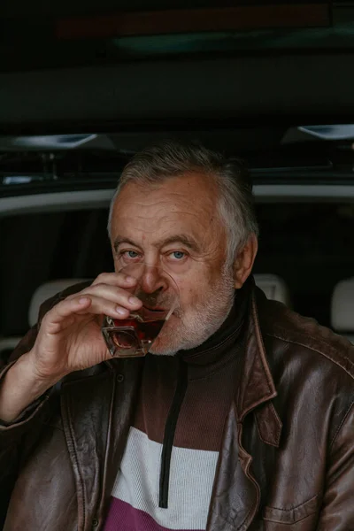 Idős Férfi Szürke Szakállal Bőrdzsekiben Whiskyt Iszik Egy Üvegpohárból Egy — Stock Fotó