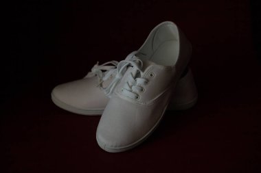 Bağcıklı iki yeni beyaz spor ayakkabı kırmızı izole bir arka planda duruyor.