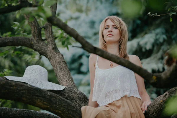 自然的肖像 穿着白色上衣的瘦小时髦的女孩坐在树枝上 — 图库照片