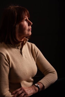 Bir fotoğraf stüdyosundaki siyah arka planda profili olan yaşlı bir kadının portresi. Dramatik ve derin hayat hikayesi. Tüm doğal kusurları korurken rötuşsuz fotoğraf