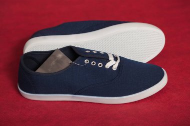 Beyaz tabanlı ve bağcıklı iki yeni mavi spor ayakkabı kırmızı izole bir arka planda duruyor.