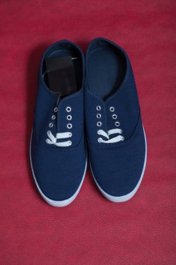 Beyaz tabanlı ve bağcıklı iki yeni mavi spor ayakkabı kırmızı izole bir arka planda duruyor.