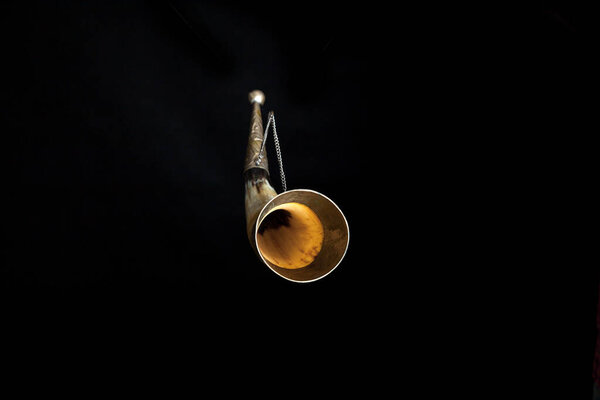 Souvenir horn for alcoholic drinks on a chain on a black background. The edges of the horn inlaid with meta