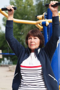 Güzel, aktif, yaşlı bir kadın oyun grubunun sokak egzersiz makinesinde fiziksel egzersiz yapıyor.