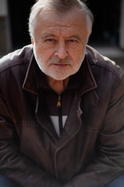 Gri sakallı bir adamın portresi. Deri ceketli ve şapkalı yaşlı adam, sonbahar günü kapanıyor.