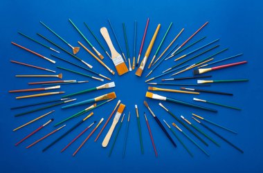 Çeşitli renk, boyut ve kıllardan oluşan fırçalar dairesel patlak desenler halinde serili. Düz çekim, mavi arkaplanda izole edilmiş.